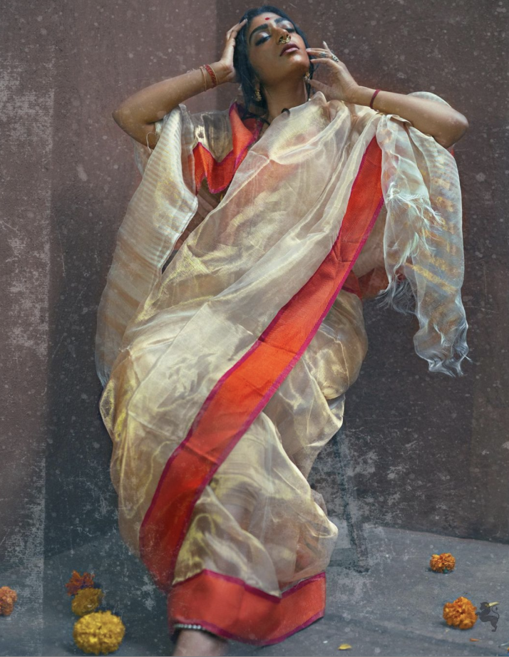 Feminine — a figure in a golden organza saree against a weathered wall